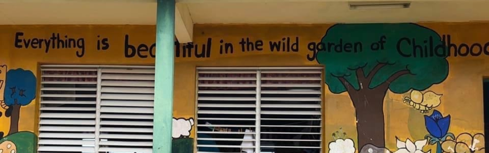 A decorative wall of a school building. It has trees, plants, and butterflies painted on it.